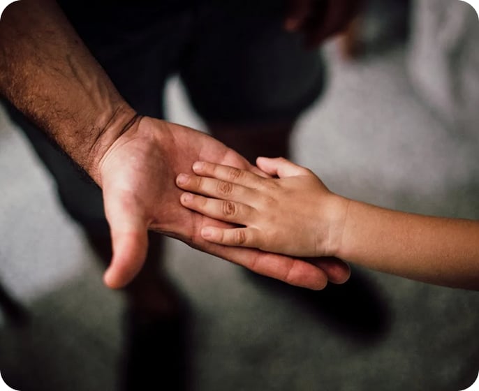 Image A child's hand rests gently on top of an adult's open palm, symbolizing connection and trust. The background is softly blurred, drawing focus to the hands.